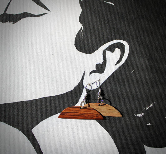 A pair of amber and ivory colored earrings hanging from a wooden board, which is attached to a wall by a chain.