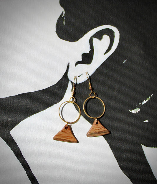 A pair of gold-colored hoop earrings with a geometric triangular design, displayed against a black background with a silhouette of a person's ear in the background.