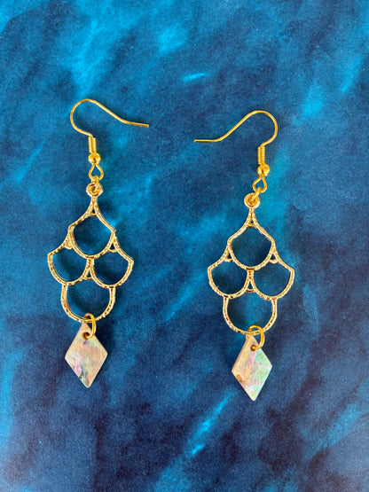 Gold earrings with geometric design on a blue textured background with Martin Guitar abalone pearl drops.