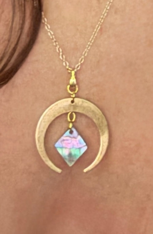 Gold crescent pendant with an abalone pearl diamond around woman's neck.