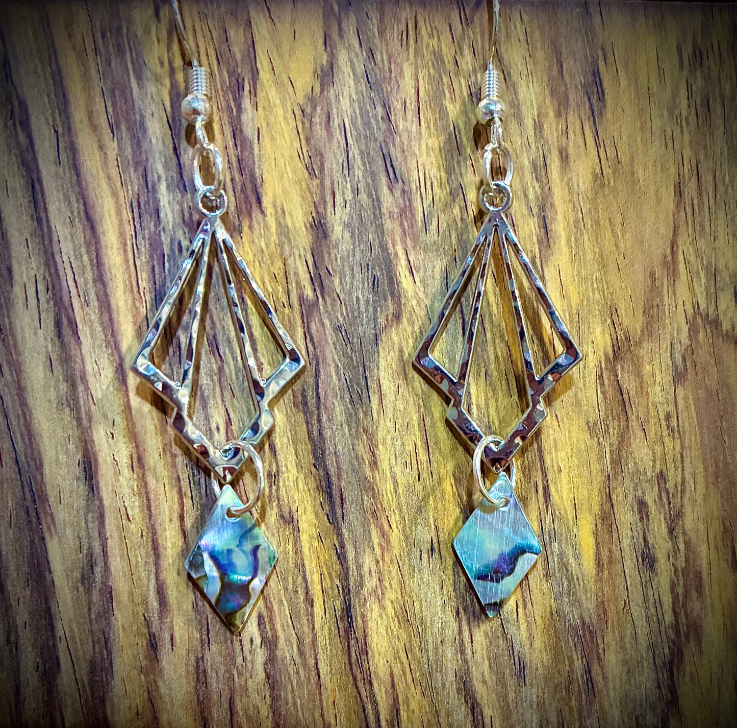 Pair of silver earrings with geometric designs and abalone pearl diamonds from Martin guitar factory on a wooden surface