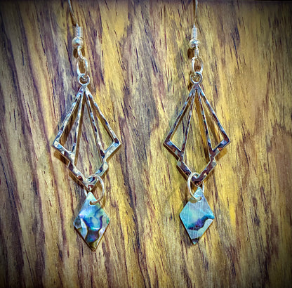 Pair of silver earrings with geometric designs and abalone pearl diamonds from Martin guitar factory on a wooden surface