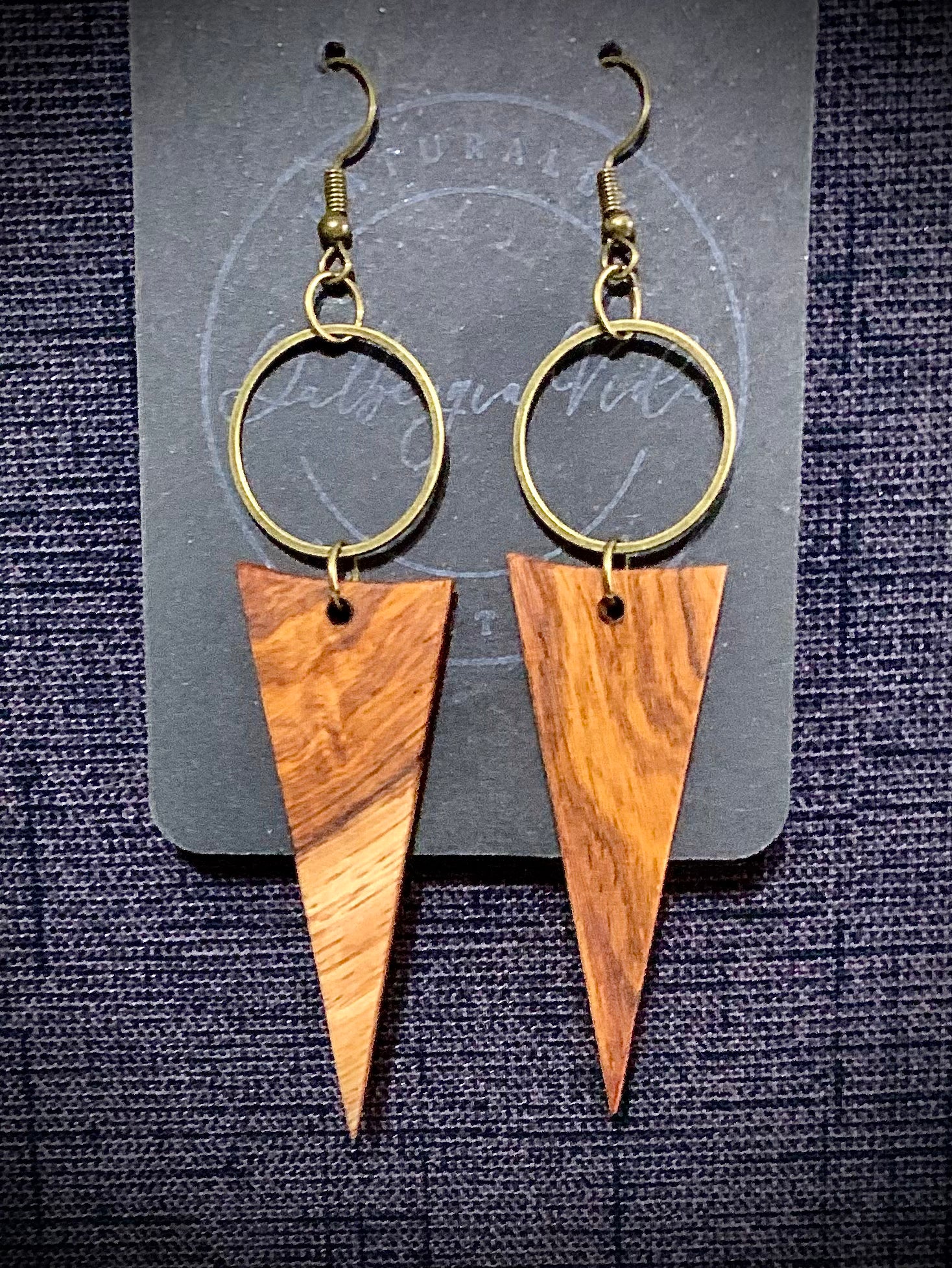 Wooden triangle earrings with gold hoop accents on a textured black background
