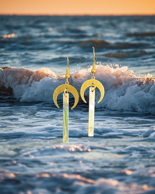 Gold earrings with crescent moon design in front of ocean waves