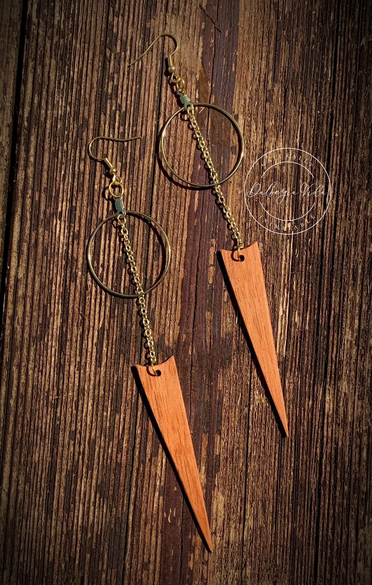 A pair of exotic guitar wood spike earrings with gold accents on a wooden surface.