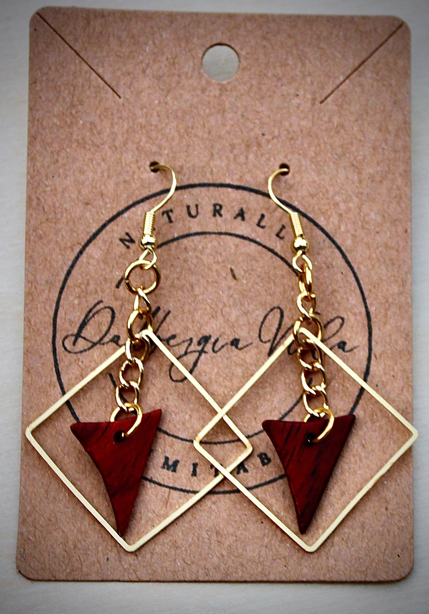 A pair of gold chain cocobolo earrings with red and brown wood coloring, displayed on a card with 'Dalbergia Vida' branding.