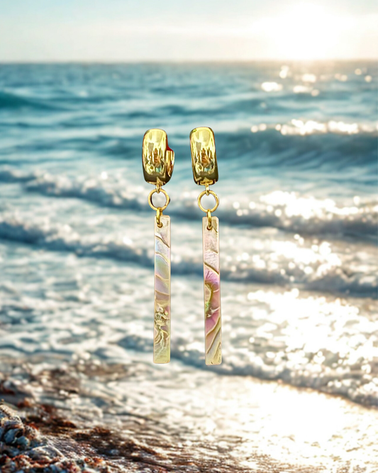 Gold earrings with marbled stones on a beach with ocean waves in the background