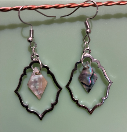 Pair of silver earrings with shell-like pendants on a green background