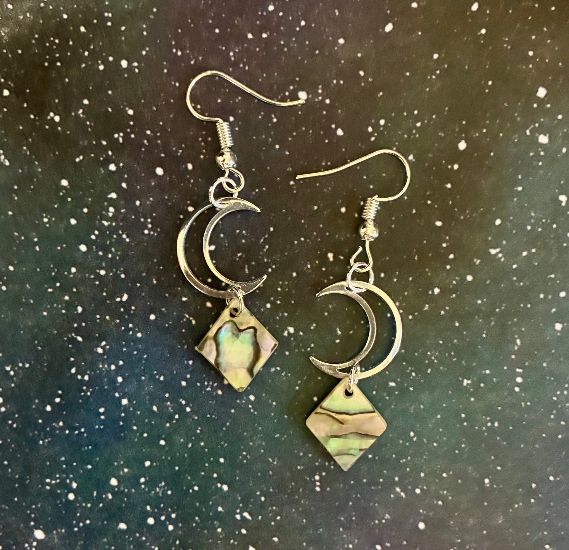Pair of earrings with moon and diamond-shaped abalone pearls on a starry night sky background