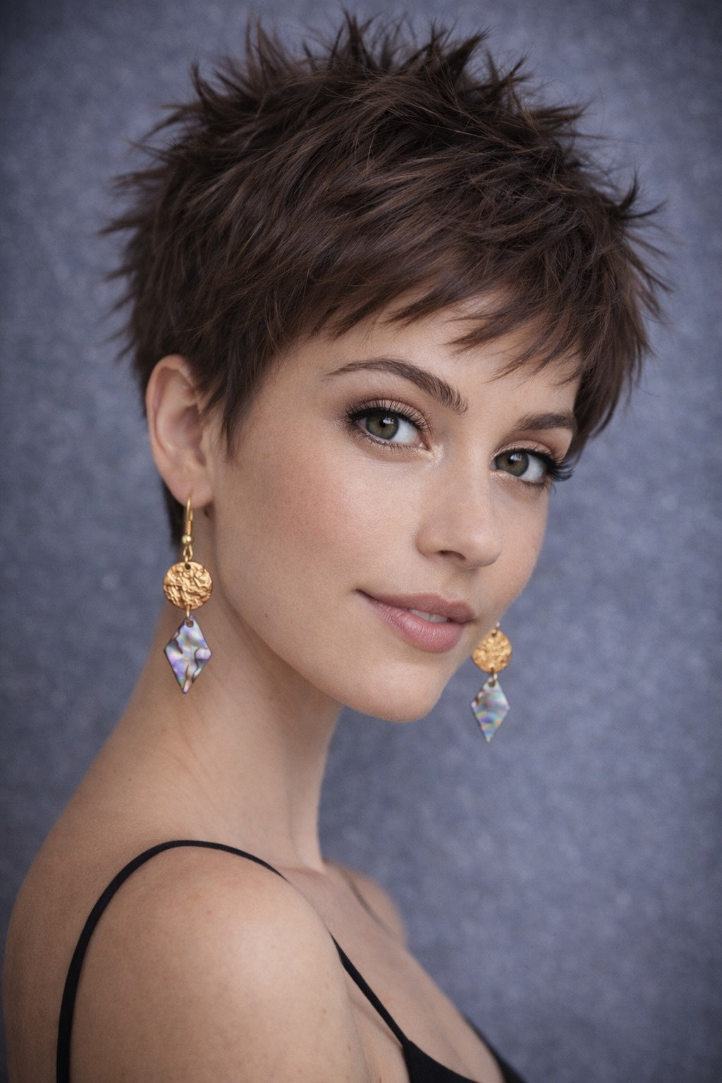 Woman with styled hair and gold and pearl earrings against a gray background