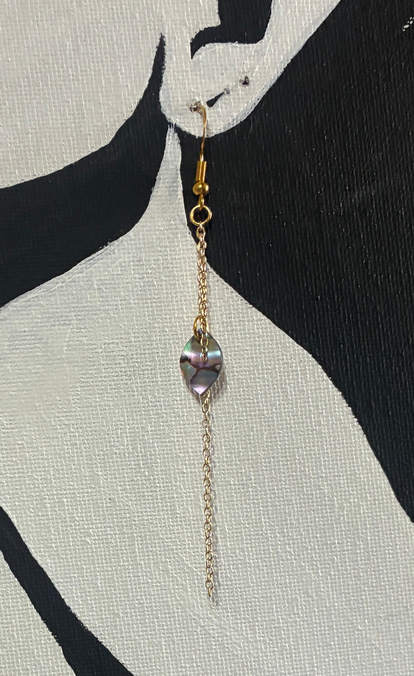 black and white painting with an earring made of gold chains and abalone pearl.