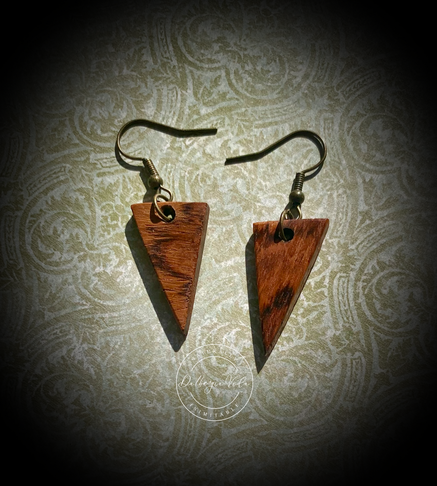Rosewood guitar wood earrings agains textured green and cream background.