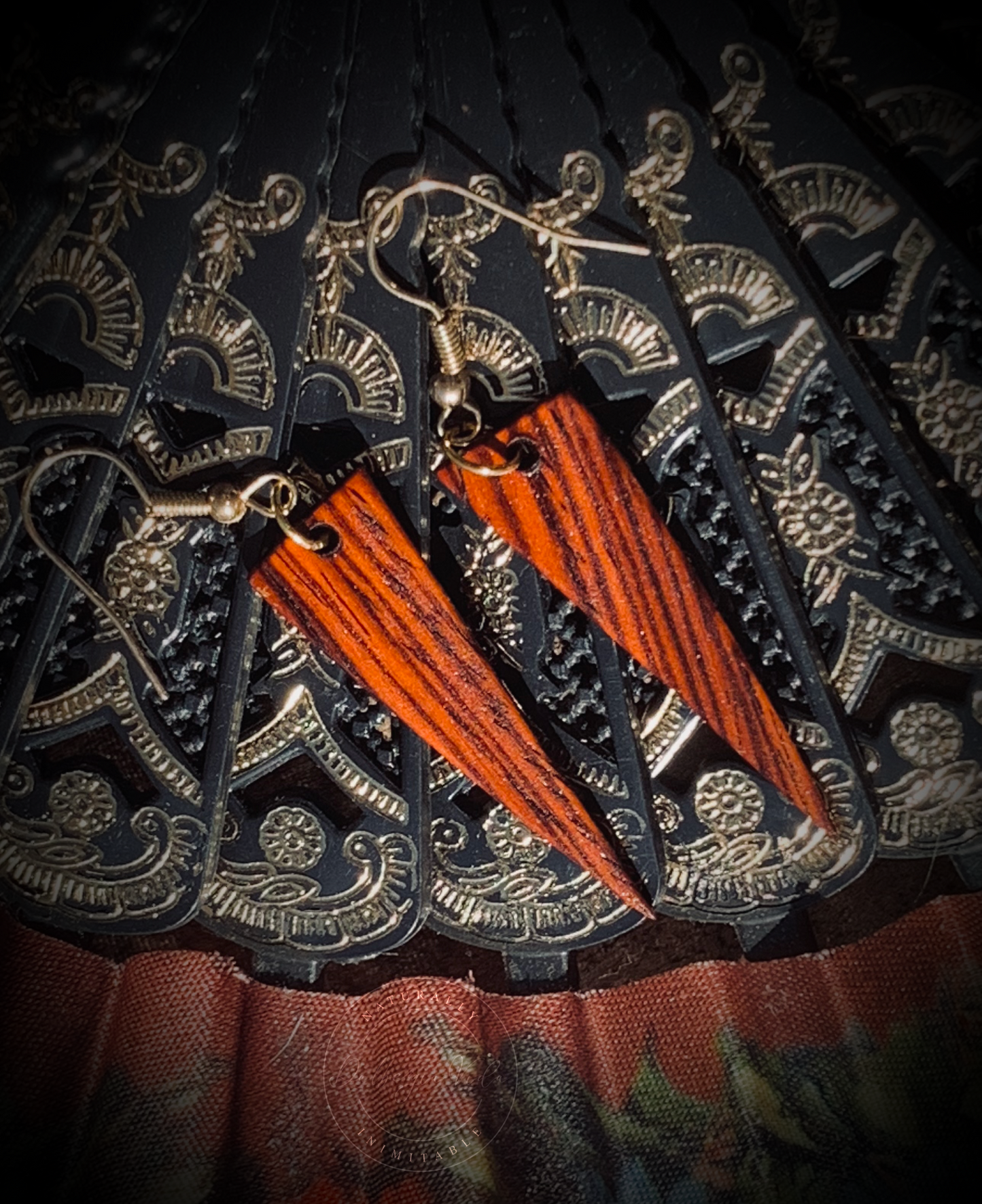 Reddish orange dagger shaped earrings against a vintage Spanish hand fan.