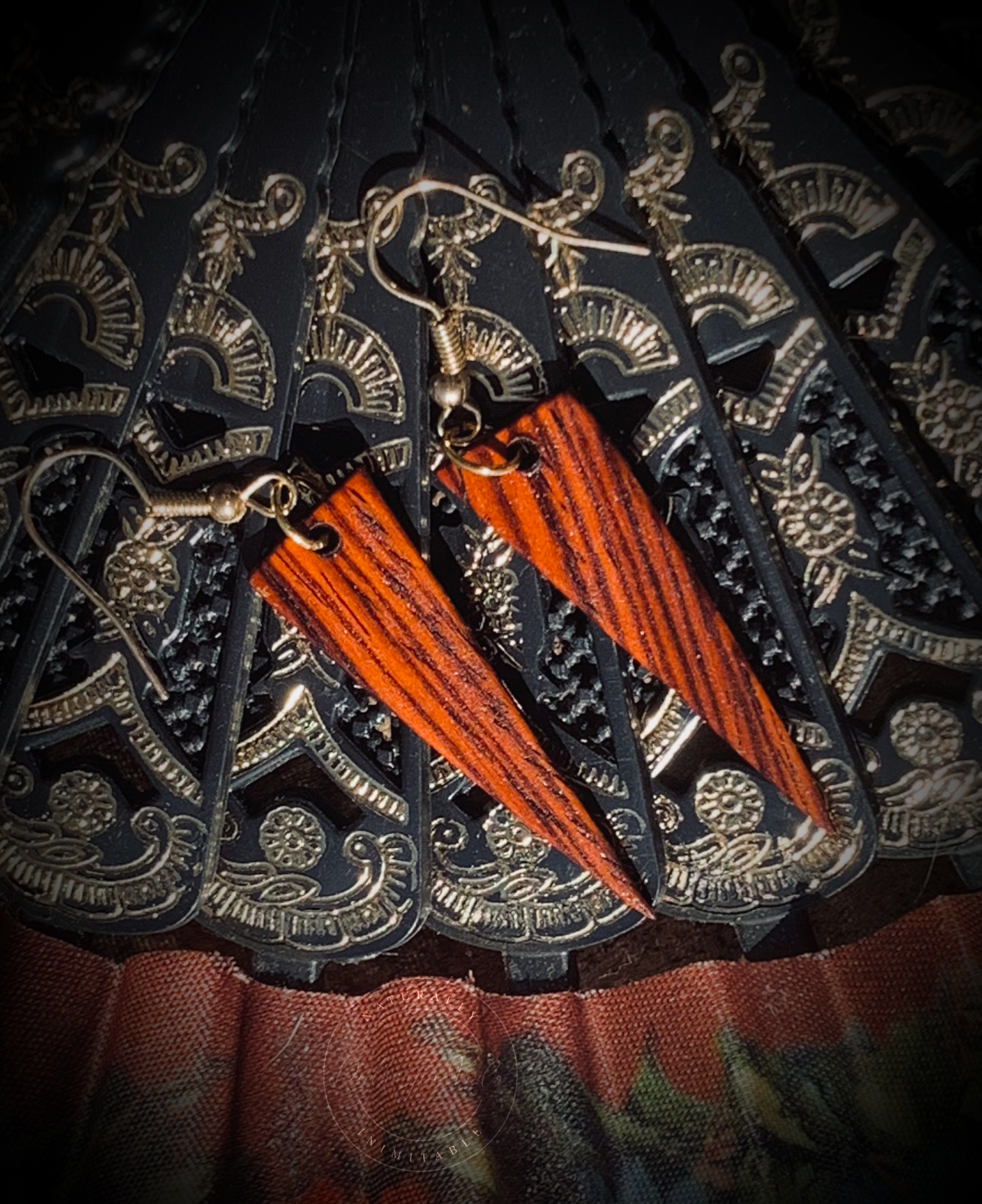 Reddish orange dagger shaped earrings against a vintage Spanish hand fan.