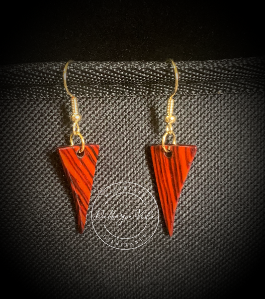 Dagger shaped Cocobolo guitar wood earrings against black background.