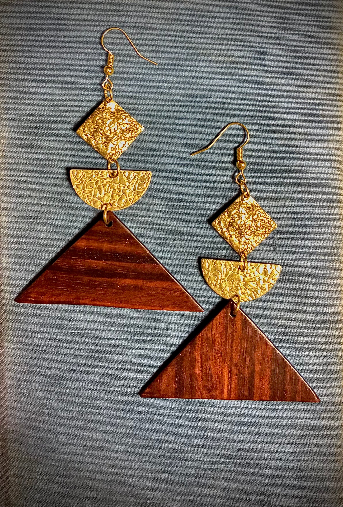 Pair of geometric earrings with hammered gold and exotic guitar wood design on a gray background