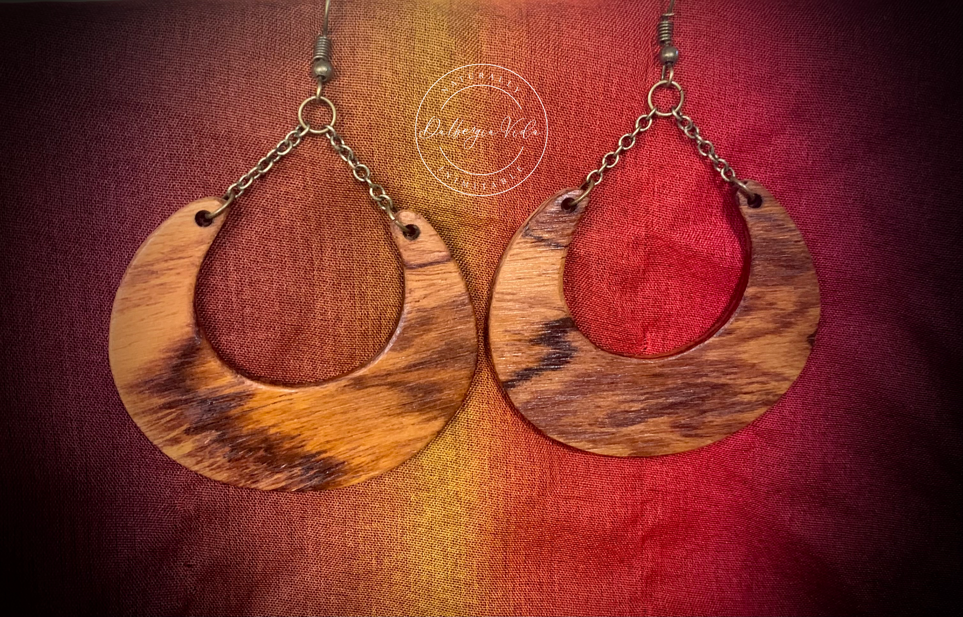 A pair of Wildwood Chain Chandelier Earrings with a boho design, featuring exotic wood and metal chains, displayed against a red and yellow textured background.
