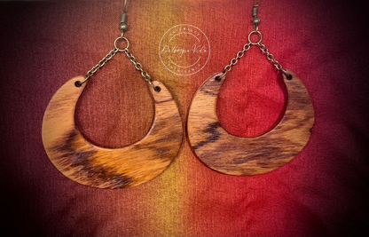 A pair of Wildwood Chain Chandelier Earrings with a boho design, featuring exotic wood and metal chains, displayed against a red and yellow textured background.