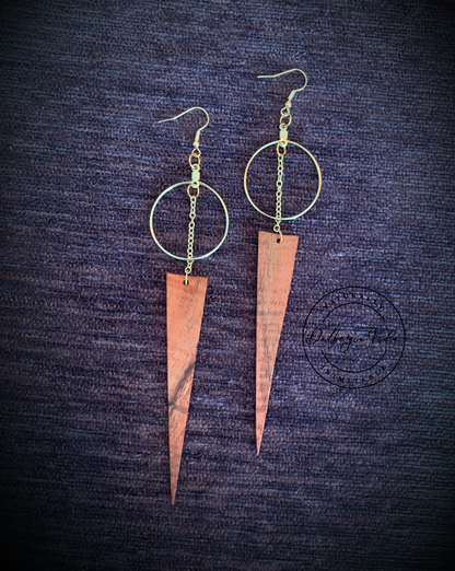 Gold hoop earrings with connecting gold chain to wild grain rosewood spear shaped wood pieces against purple carpet background. Martin guitar factory.