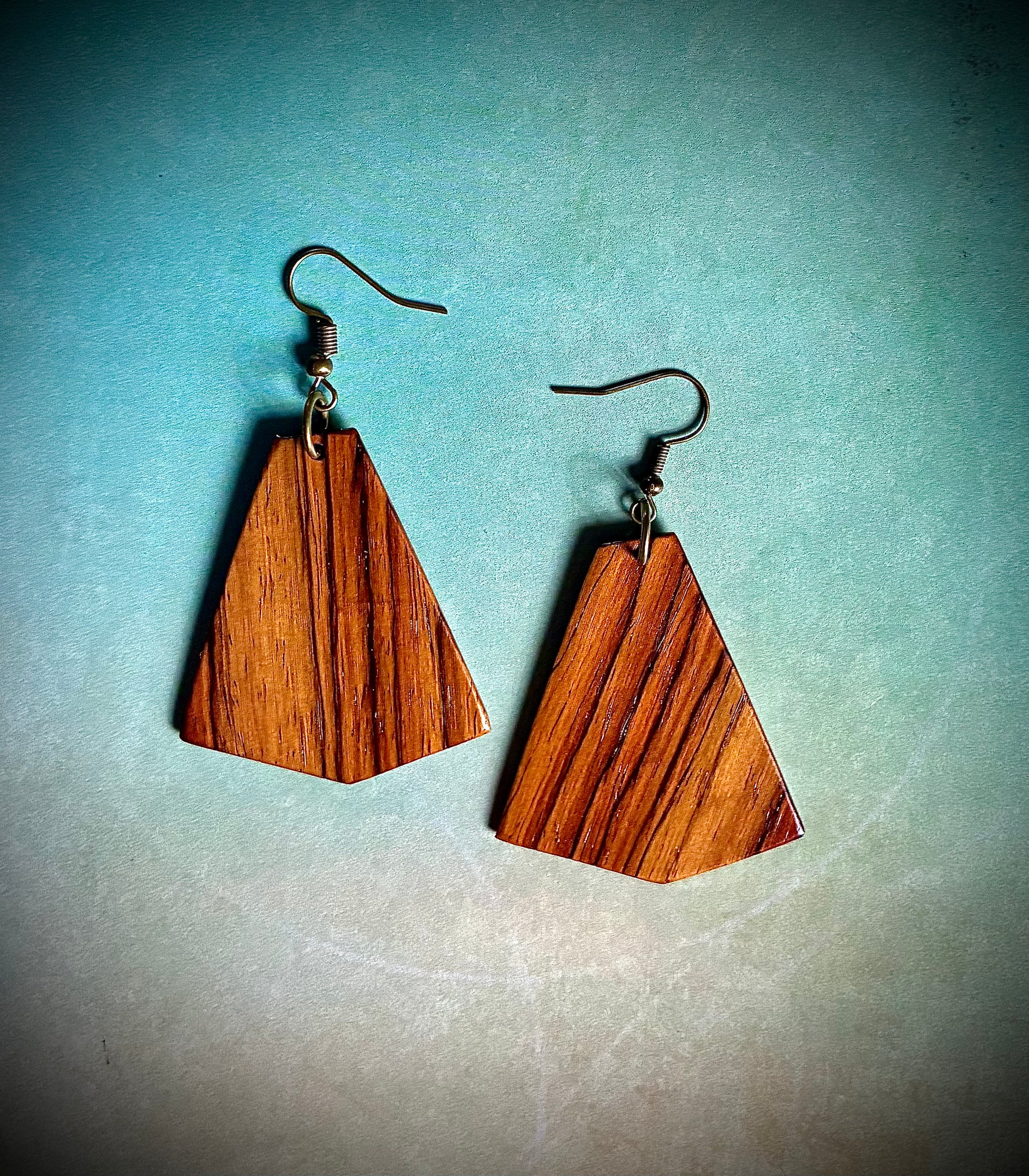 Wooden triangle-shaped earrings made from Martin Guitar exotic guitar wood on a gradient blue and beige background